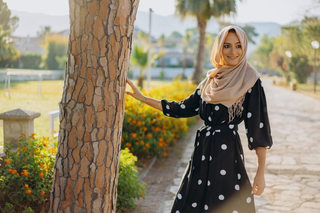 A cheerful woman in a fashionable polka dot dress and hijab enjoying a sunny day outside.