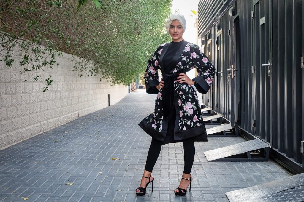 Stylish woman wearing a floral abaya and hijab, confidently posing outdoors.